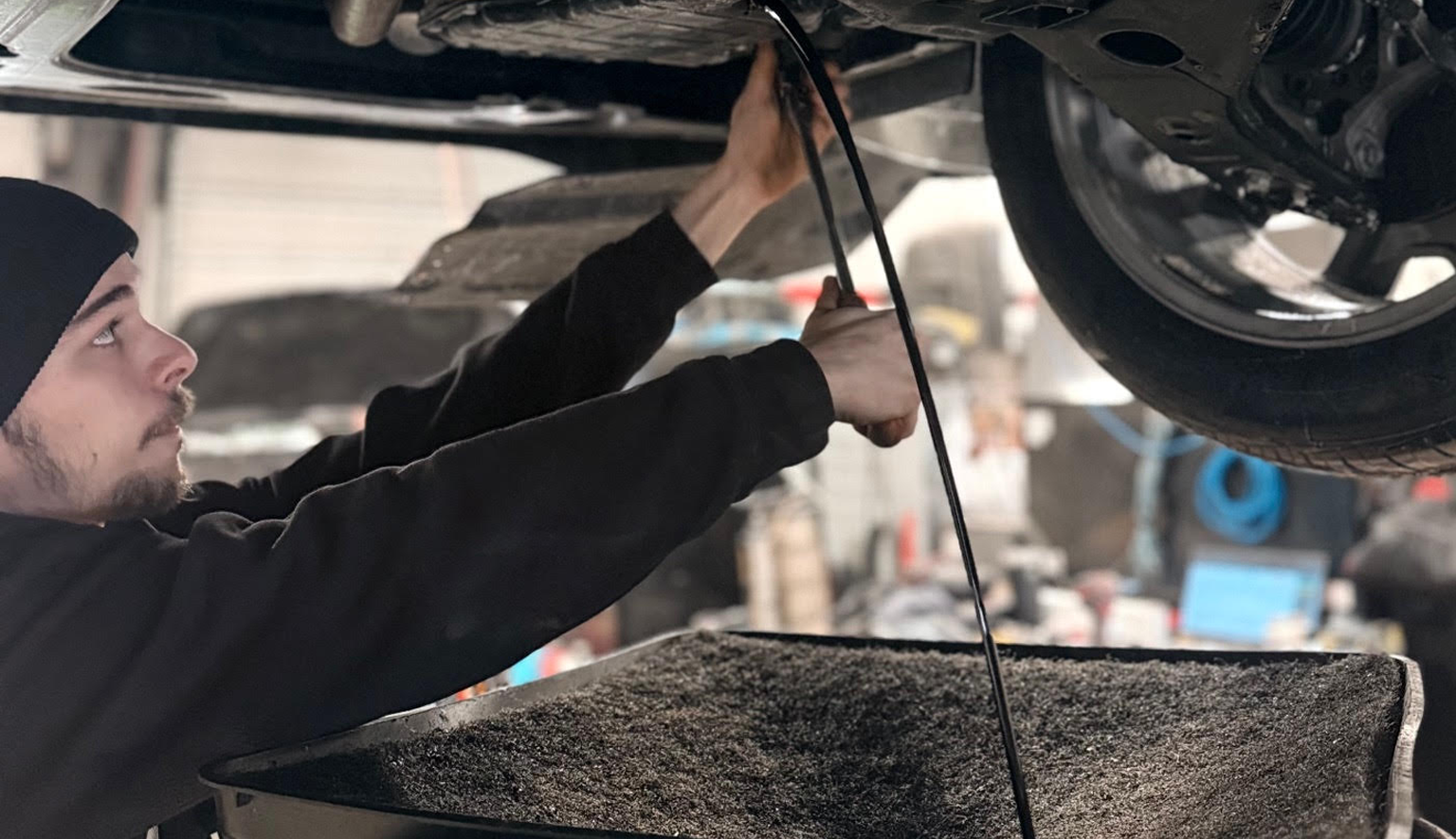 Technician performing engine oil and filter change service on a vehicle